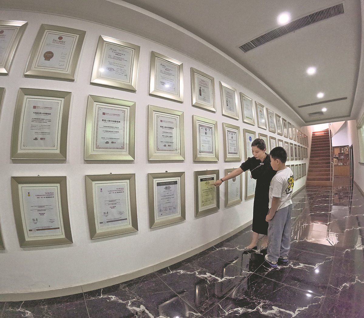 He Yangyang menunjukkan anugerah-anugerah pertandingan antarabangsa yang dimenangi wain keluaran kilangnya kepada anaknya. (foto: Yan Dongjie/China Daily)
