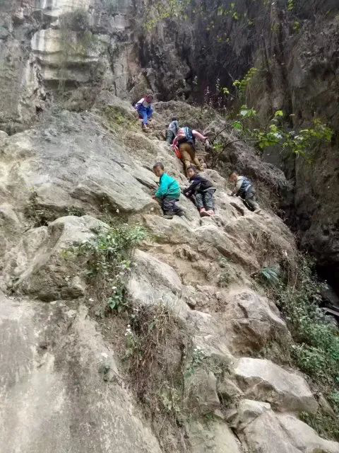 Orang dewasa menemani pelajar memanjat bukit untuk ke sekolah. (Foto fail)