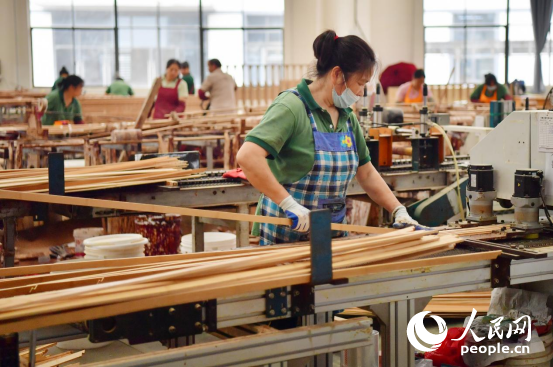 Para pekerja sedang memasang bod buluh bersalut plastik di bengkel pemprosesan. (People’s Daily Online/Shi Yu)